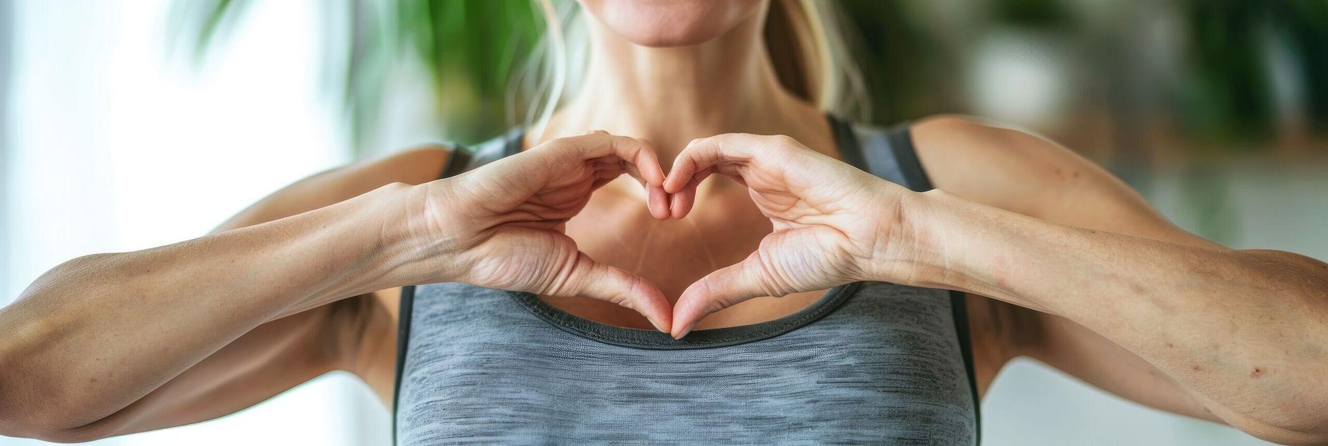 Eine Frau formt mit ihren Händen ein Herz vor ihrer Brust in sportlicher Kleidung.