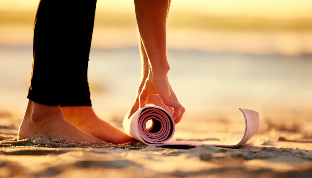 Eine Frau rollt eine Yogamatte am Strand aus, um mit ihrem Zen-Training und Stretching zu beginnen.