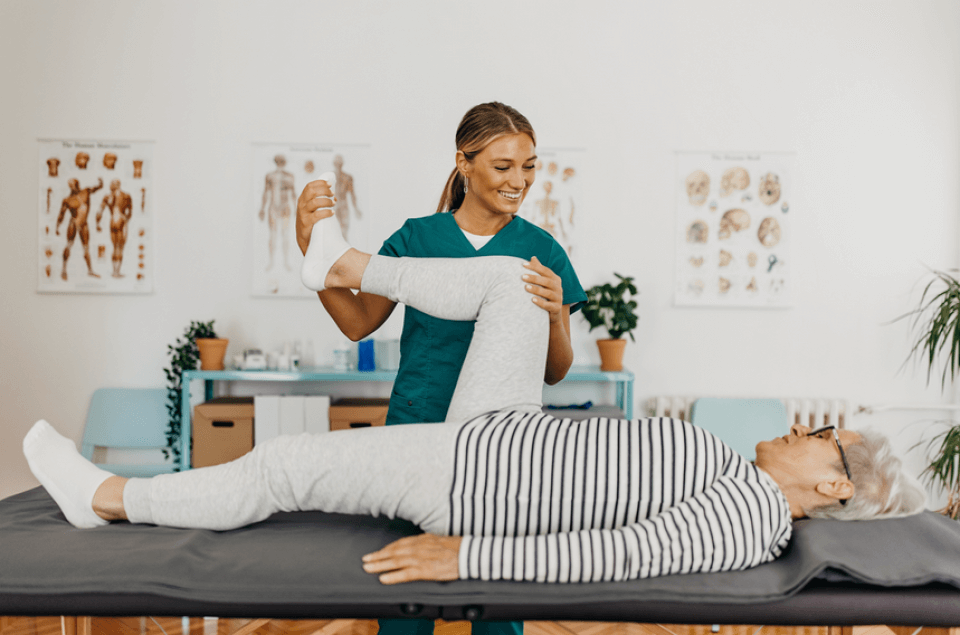 Eine Physiotherapeutin hilft einem älteren Mann bei Übungen auf einer Liege im Krankengymnastikraum.